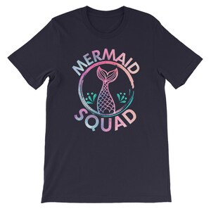 May include: A navy blue t-shirt with a pink, blue, and green watercolor design of a mermaid tail inside a circle with the text "Mermaid Squad".