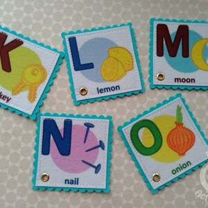 K&ouml;nnte beinhalten: F&uuml;nf Filz-Alphabet-Karten mit einem Buchstaben, einem Bild und einem Wort. Die Buchstaben sind K, L, M, N und O. Die Bilder sind ein Schl&uuml;ssel, eine Zitrone, ein Mond, ein Nagel und eine Zwiebel.