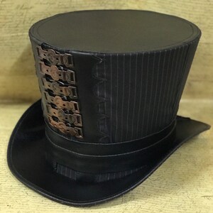 May include: A black top hat with a pinstripe pattern and a band of metal accents around the crown.