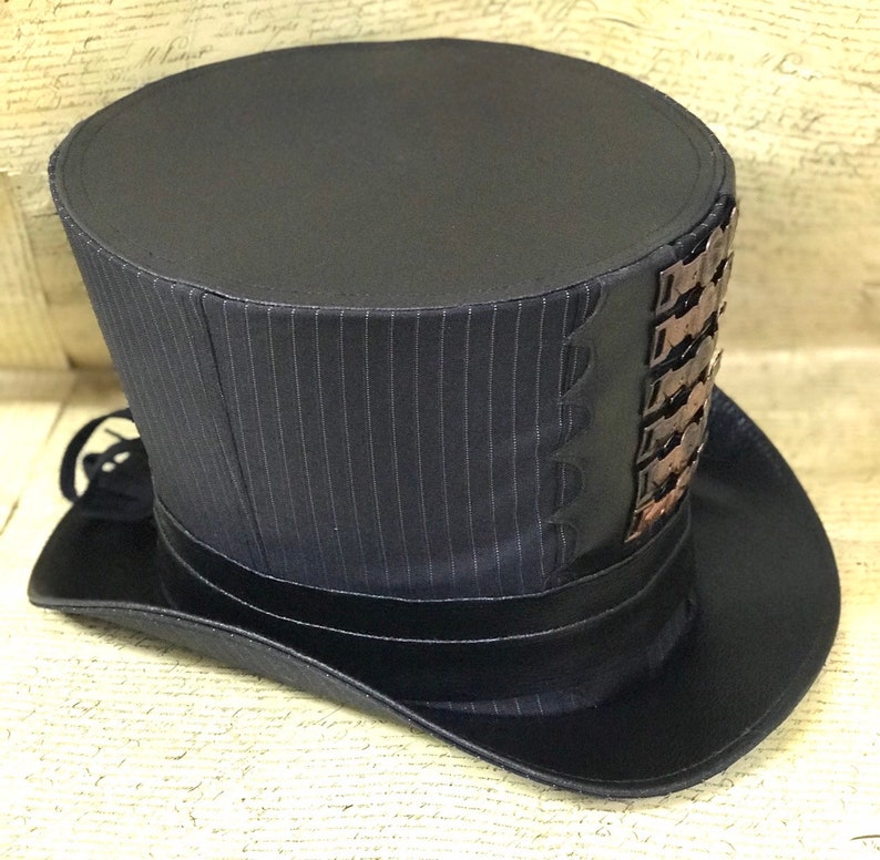 May include: A black top hat with a pinstripe pattern and a decorative band of metal accents. The hat has a wide brim and a tall crown.