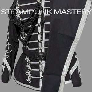 Può includere: Completo giacca e pantaloni neri in stile militare con finiture e dettagli argentati. La giacca presenta bottoni argentati decorativi, una cintura nera con fibbia a teschio e ricami bianchi. Il testo "STEAMPUNK MASTERY" è visibile.
