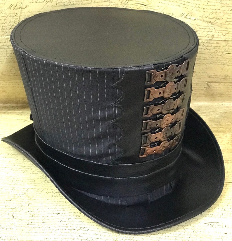 May include: A black top hat with a pinstripe pattern and a band of black leather around the base. The hat has a series of decorative metal buckles on the side.