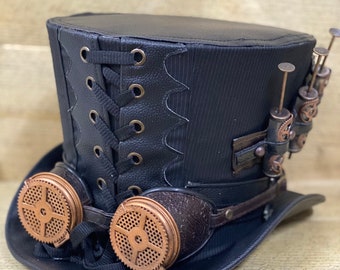 Peut inclure: Un chapeau haut de forme noir avec un design steampunk. Le chapeau a un bandeau en cuir noir avec un motif d'engrenage de couleur cuivre. Le chapeau a également une paire de lunettes avec des montures de couleur cuivre et des sangles en cuir noir.