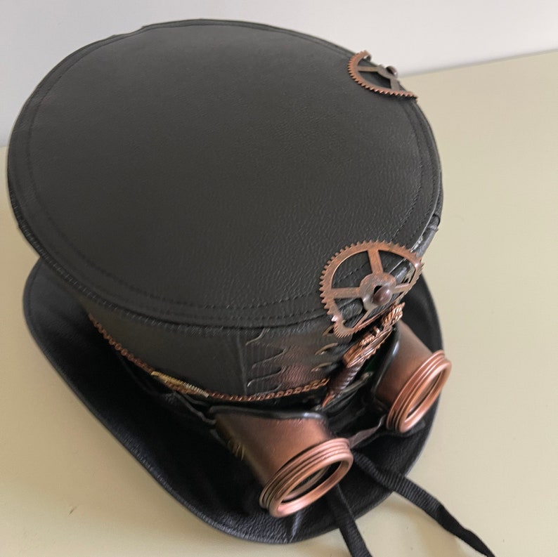 Pu&ograve; includere: Cappello a cilindro steampunk nero con occhiali e ingranaggi color rame. Il cappello presenta una corona rotonda e un'ampia tesa. Gli occhiali sono attaccati al cappello con elementi metallici decorativi. Un accessorio elegante per cosplay o eventi a tema.
