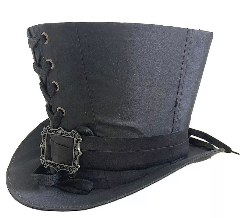 Op de afbeelding: Een zwarte hoge hoed met een brede rand en een hoge, cilindrische kroon. De hoed heeft een decoratieve band rond de basis en een zilverkleurige gesp. De zijkant van de hoed heeft een veterdetail.