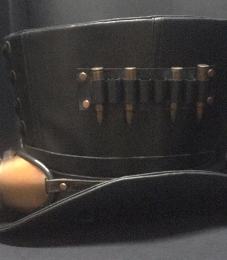 Puede incluir: Un sombrero de copa de cuero negro con una banda de lat&oacute;n y un portamuniciones de cuero con cinco casquillos de bala.