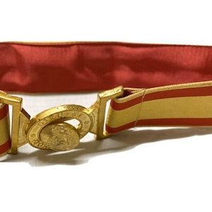 Può includere: Una fibbia dorata per cintura con un designo circolare e una cintura a righe rosse e dorate.