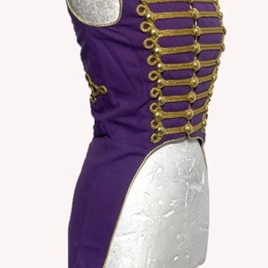 May include: A purple, sleeveless, tailcoat-style vest with gold trim and buttons. The vest has a high collar and a long, pointed tail.