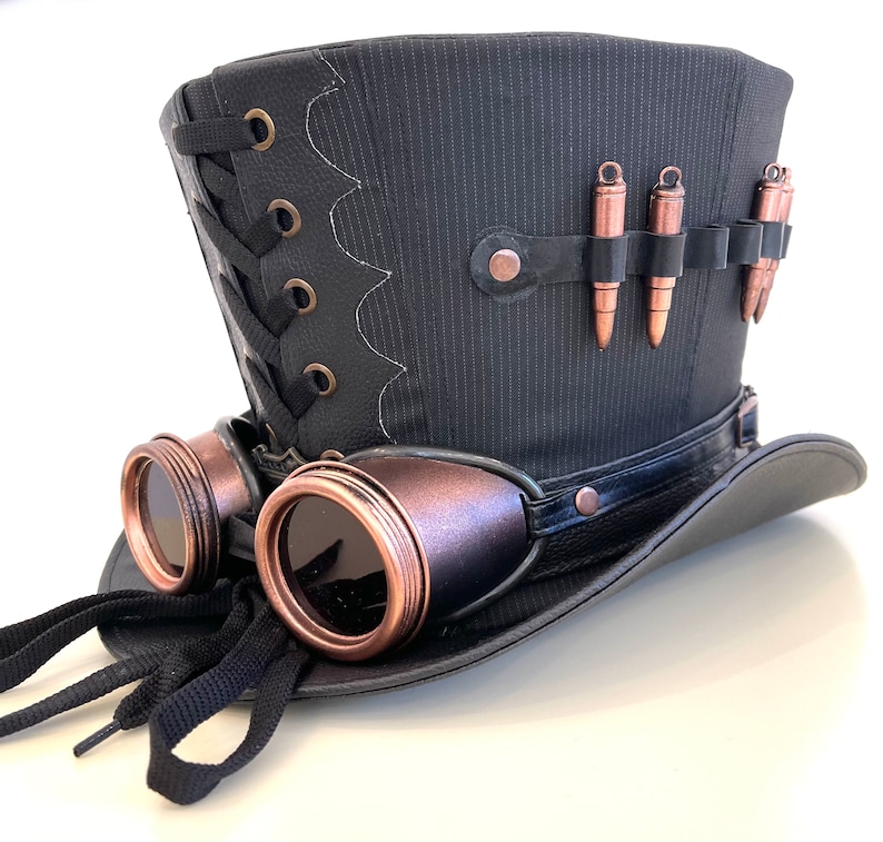 May include: A black top hat with a black leather band and a pair of copper-colored goggles attached to the side. The hat has a black and white striped pattern and a row of copper-colored bullets on the top.