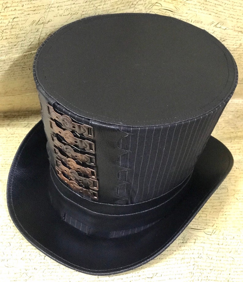 May include: A black top hat with a striped fabric band and a row of metal accents. The hat has a wide brim and a tall, cylindrical crown.
