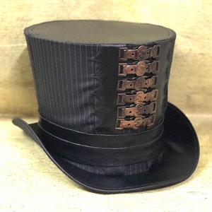 May include: A black top hat with a striped fabric crown and a black leather band. The hat has a series of decorative metal buckles on the side.