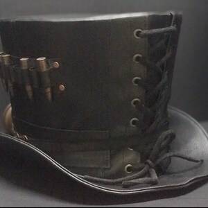 Puede incluir: Un sombrero de copa de cuero negro con un detalle de encaje en el lateral y una banda de balas alrededor de la base.