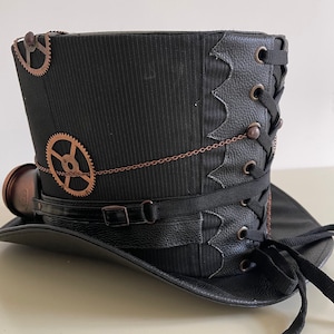 Pu&ograve; includere: Un cappello a cilindro steampunk nero con ingranaggi color rame e una piccola lente rotonda. Il cappello presenta una fascia in pelle nera con fibbia, un design allacciato e una catena decorativa. Il cappello &egrave; realizzato in tessuto a righe.