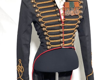 May include: A black tailcoat jacket with gold braid trim and red piping. The jacket has a stand-up collar and a row of buttons down the front. There are decorative gold braid knots on the sleeves and back of the jacket.