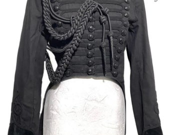 May include: A black steampunk-style jacket with a long tail, featuring a high collar, decorative buttons, and a braided cord detail. The jacket has a velvet trim and is displayed on a white mannequin.