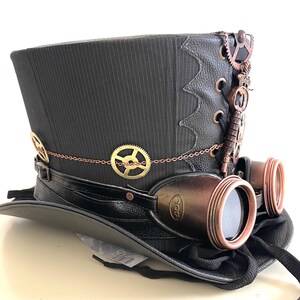 Pu&ograve; includere: Cappello a cilindro steampunk a righe nere con occhiali protettivi attaccati. Il cappello presenta ingranaggi decorativi in bronzo, una chiave e una catena. Gli occhiali hanno una montatura in bronzo e lenti scure.