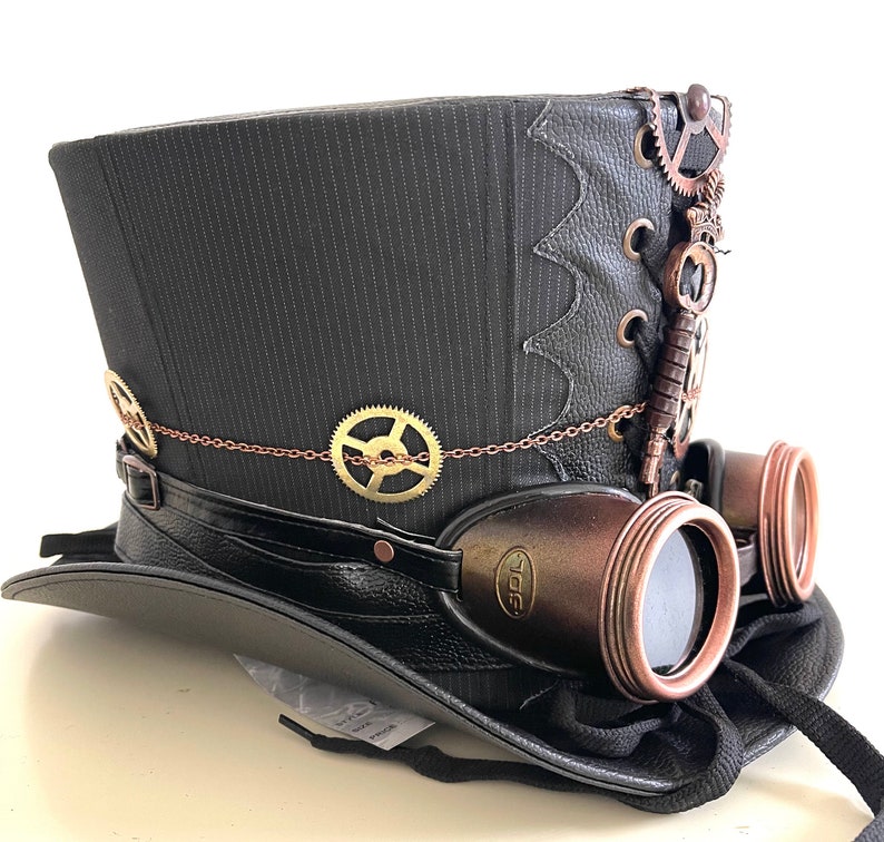 Pu&ograve; includere: Cappello a cilindro steampunk a righe nere con occhiali protettivi attaccati. Il cappello presenta ingranaggi decorativi in bronzo, una chiave e una catena. Gli occhiali hanno una montatura in bronzo e lenti scure.