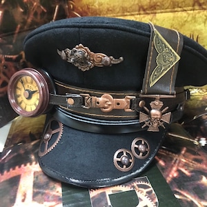 Può includere: Un cappello in feltro nero con un'ampia tesa e una fascia in pelle. Il cappello presenta una varietà di elementi decorativi, tra cui un orologio, ingranaggi e un teschio con ossa incrociate. Il cappello è un accessorio in stile steampunk.