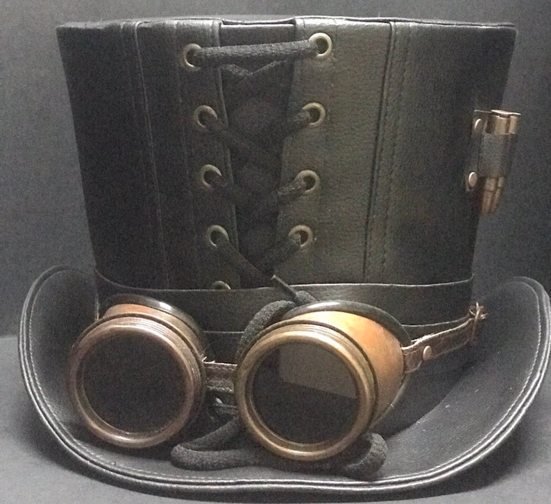Puede incluir: Un sombrero de copa de cuero negro con un detalle de encaje y un par de gafas de lat&oacute;n unidas al borde.