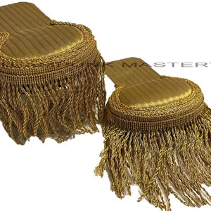 Puede incluir: Dos hombreras doradas con flecos. Las hombreras están hechas de una tela con un sutil patrón de rayas. Los flecos son un grueso fleco dorado.