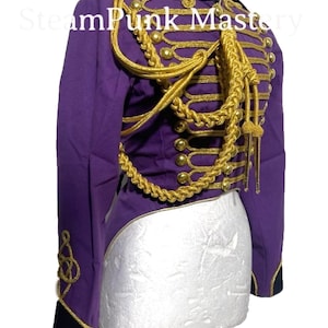 Puede incluir: Chaqueta de estilo militar de color morado y dorado con botones y ribetes dorados. La chaqueta tiene una cola larga en la parte posterior y un cuello alto.