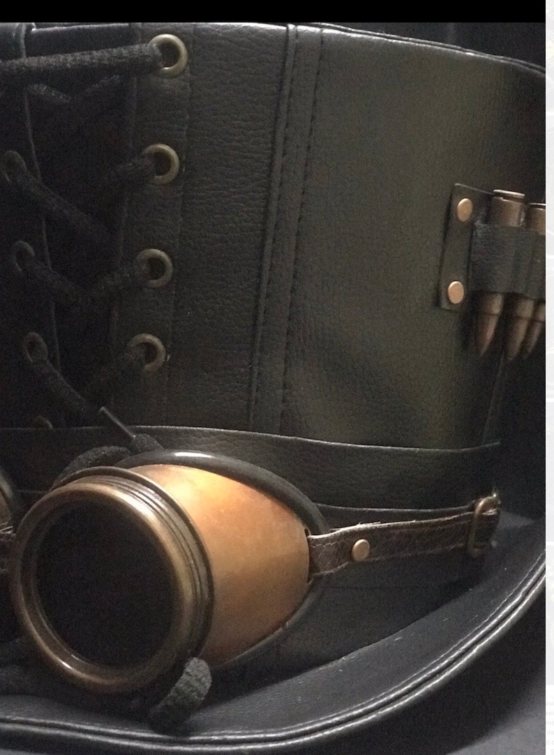 Puede incluir: Un sombrero de copa de cuero negro con una banda de cuero marr&oacute;n y gafas de lat&oacute;n. El sombrero tiene un detalle de encaje y una fila de balas de lat&oacute;n en el lateral.