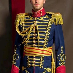 Può includere: Giacca blu navy in stile militare con decorazioni dorate, tra cui spalline, bottoni e ricami decorativi. La giacca presenta dettagli rossi sul colletto e sui polsini e una fascia dorata e rossa. È un costume.