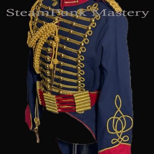 May include: A blue military-style jacket with gold braid trim and buttons. The jacket has a red collar and a long tail. The jacket is on a mannequin.
