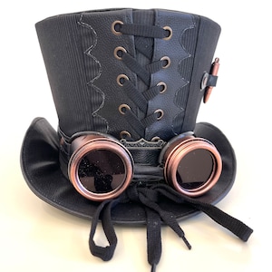 May include: A black top hat with a black lace-up detail and a pair of copper-colored goggles attached to the front. The hat has a black band around the base and a black ribbon tied at the front.
