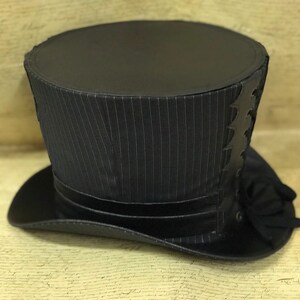 May include: A black top hat with a pinstripe pattern and a black leather trim. The hat has a tall, cylindrical crown and a wide brim.