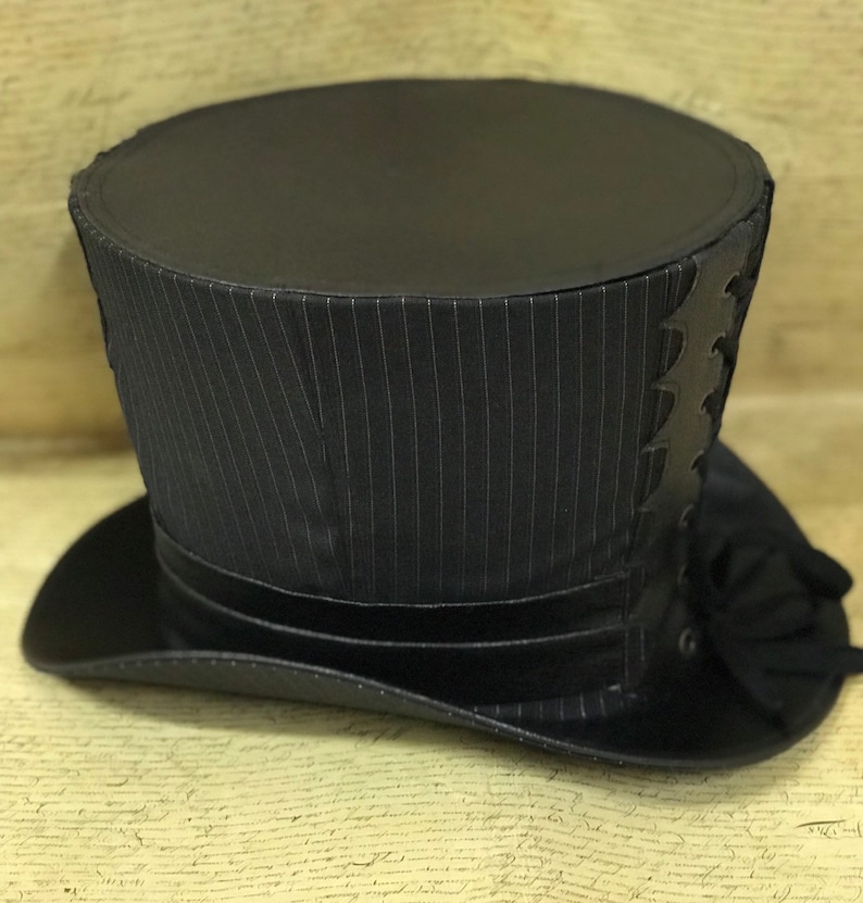 May include: A black top hat with a pinstripe pattern and a black leather trim. The hat has a tall, cylindrical crown and a wide brim.