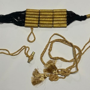 May include: A gold and black tassel necklace with a decorative gold chain and a tassel on each end.