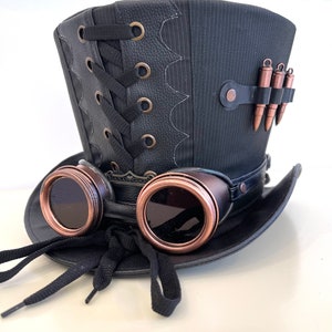 May include: A black top hat with a leather band and a lace-up detail. The hat has a pair of goggles attached to the front, with copper-colored frames and dark lenses. There are also several small, copper-colored bullet casings attached to the side of the hat.