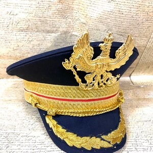 May include: A navy blue military style hat with a gold braid trim and a gold eagle emblem on the front.