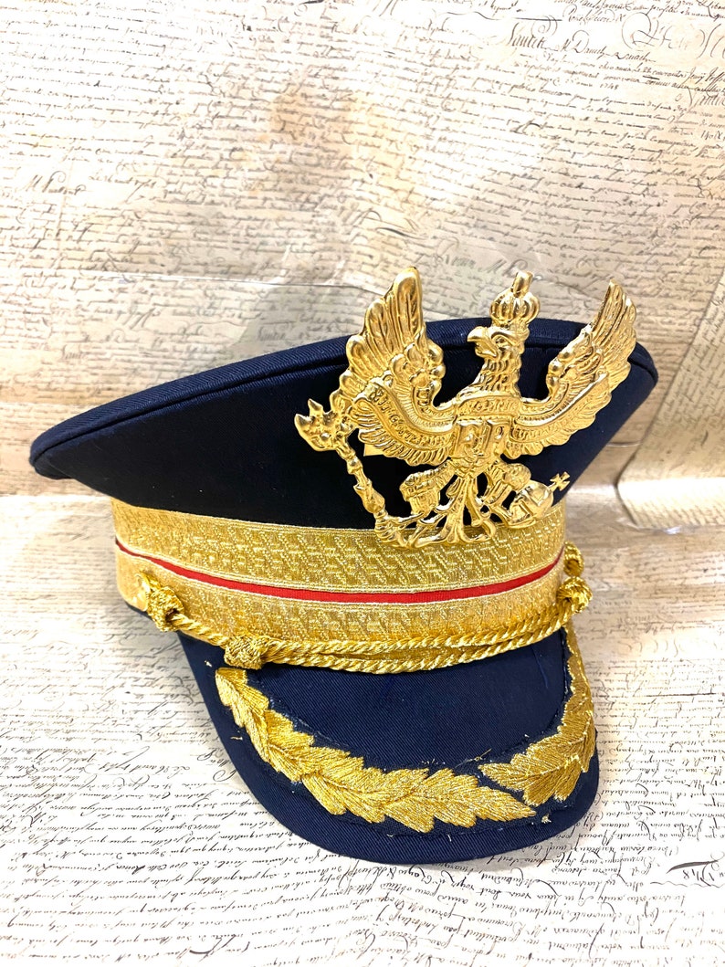 May include: A navy blue military style hat with a gold braid trim and a gold eagle emblem on the front.