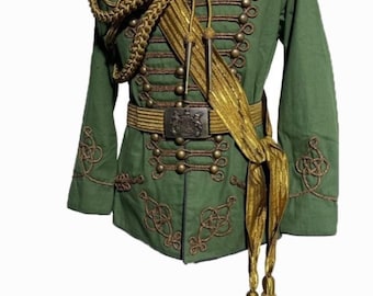 May include: A green military-style jacket with gold trim and buttons. The jacket has a high collar and is decorated with intricate gold embroidery. The jacket is worn over a white shirt with a black tie.