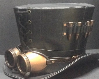Peut inclure: Un chapeau haut de forme en cuir noir avec une bande en cuir noir et des lunettes. Le chapeau a une bande de douilles de balles en laiton sur le côté.