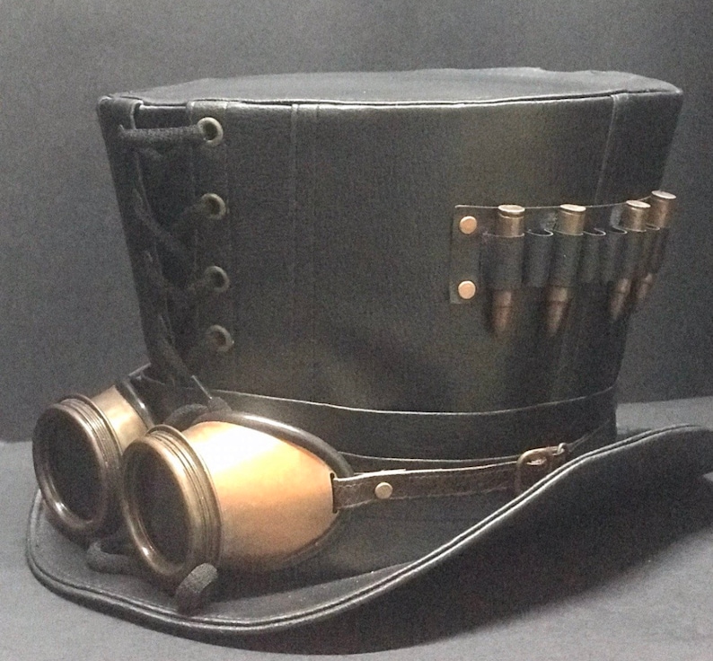 Puede incluir: Un sombrero de copa de cuero negro con una banda de cuero negro y gafas. El sombrero tiene una banda de casquillos de bala de lat&oacute;n en el lateral.