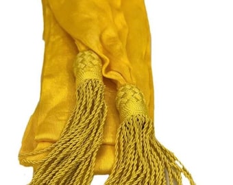 May include: A yellow sash with two tassels. The sash is made of a soft, silky fabric and has a smooth, even texture. The tassels are made of a thick, braided cord and are approximately 10 inches long.