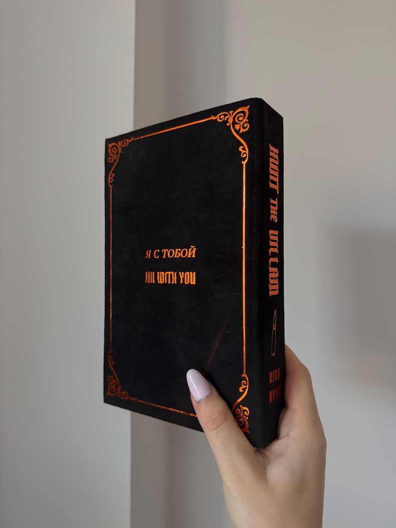 May include: Black book with gold-colored accents and text. The book's spine reads "HUNT THE VILLAIN" vertically. The front of the book has text in both English and Cyrillic script. Decorative gold-colored filigree borders the edges.