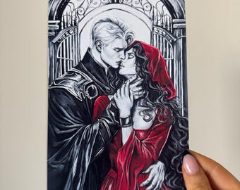 May include: Illustration of a couple embracing, set against a black and white arched gate background. The man has white hair and wears a black coat. The woman wears a red hooded dress. The artwork is held by a hand.
