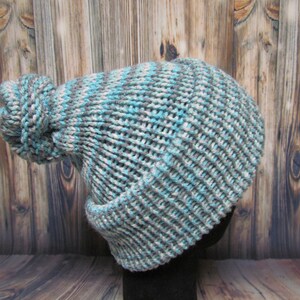 May include: A blue and gray knitted beanie with a large pom pom on top.
