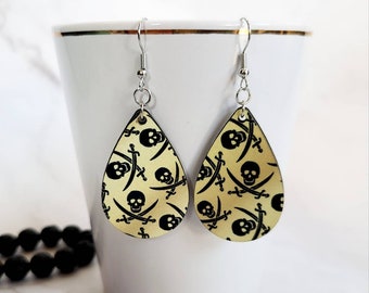 May include: A pair of teardrop-shaped earrings with a gold background and a black skull and crossbones pattern.