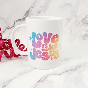 May include: White ceramic coffee mug with a rainbow gradient design that says "Love like Jesus" in a retro font.
