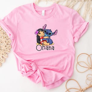 May include: Pink t-shirt with a graphic of Stitch from Lilo & Stitch hugging Lilo. The text "Ohana" is printed below the graphic.