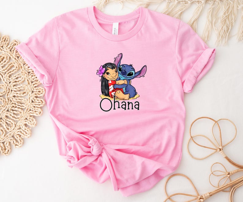 May include: Pink t-shirt with a graphic of Stitch from Lilo & Stitch hugging Lilo. The text "Ohana" is printed below the graphic.