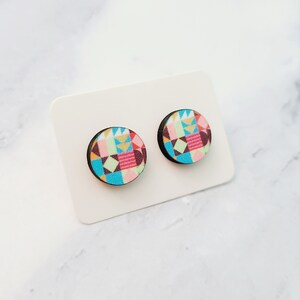 May include: A pair of colourful geometric patterned wooden stud earrings. The earrings are round and have a black backing.