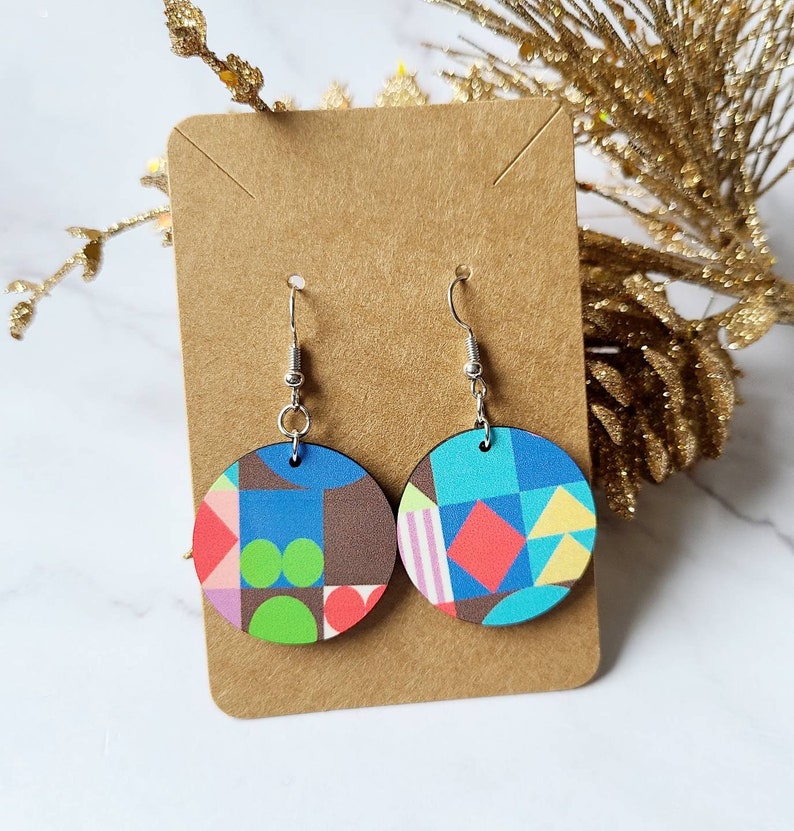 May include: A pair of round wooden earrings with a geometric pattern in shades of blue, green, pink, red, and yellow. The earrings are hanging from silver hooks.