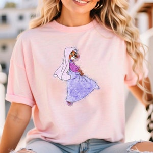 Op de afbeelding: Een roze T-shirt met een aquarel-illustratie van een cartoonvos die een paarse jurk en een witte sluier draagt.