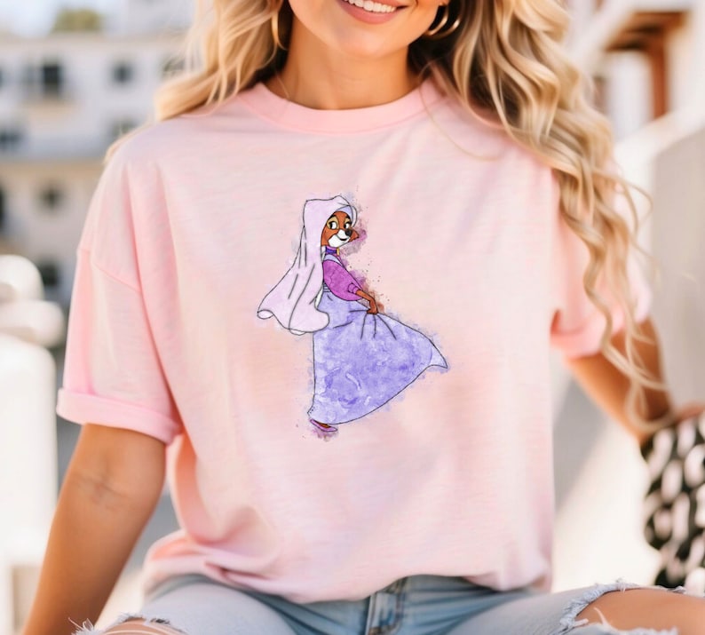Op de afbeelding: Een roze T-shirt met een aquarel-illustratie van een cartoonvos die een paarse jurk en een witte sluier draagt.